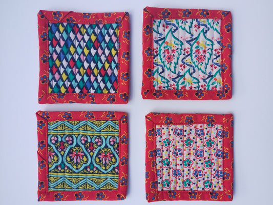 Set of four square coasters, each with a different colorful pattern but the same colors, and a matching red patterned border. The coasters are quilted with tight vertical lines.